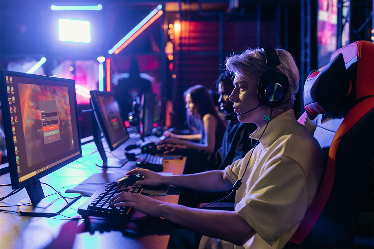 Um garoto em um ambiente gamer, sentado em uma cadeira gamer com fones de ouvido em frente ao computador.